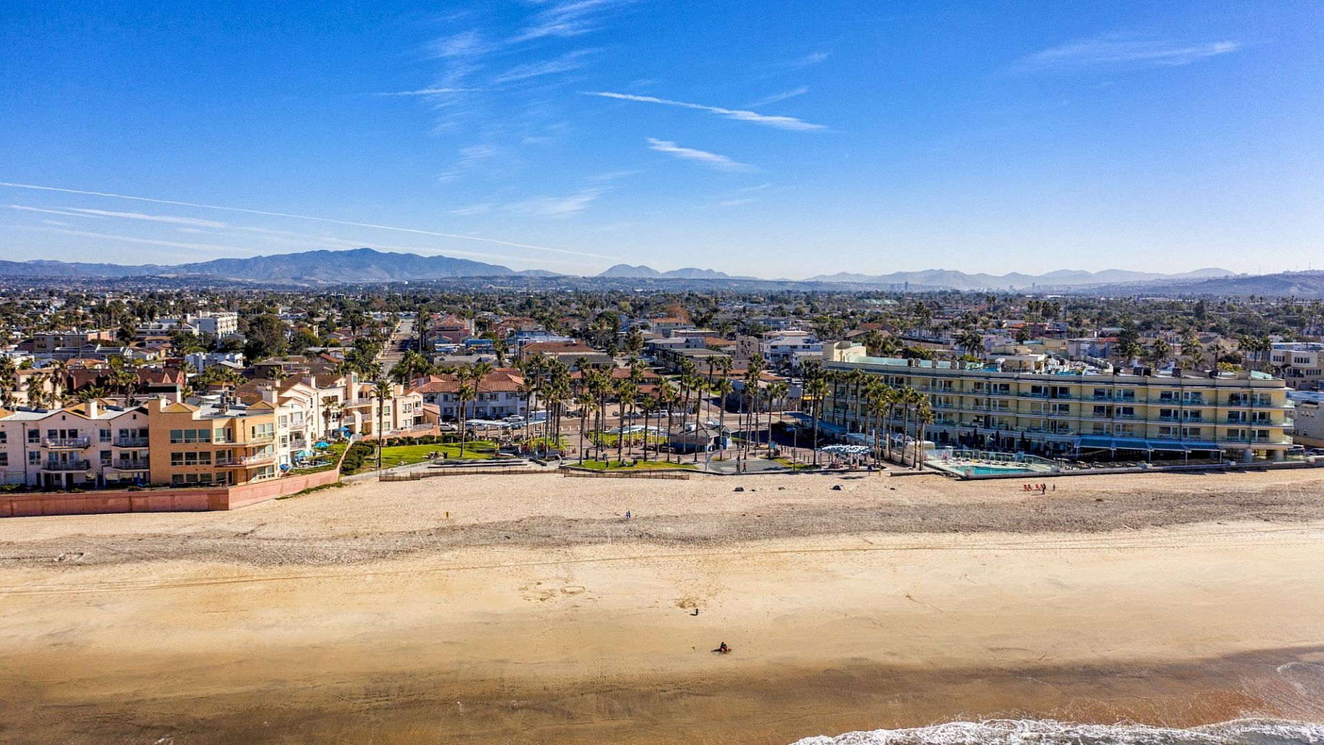 The image shows a coastal town with sandy beaches, waves, buildings, and a mountainous background under a clear blue sky, ending the sentence.