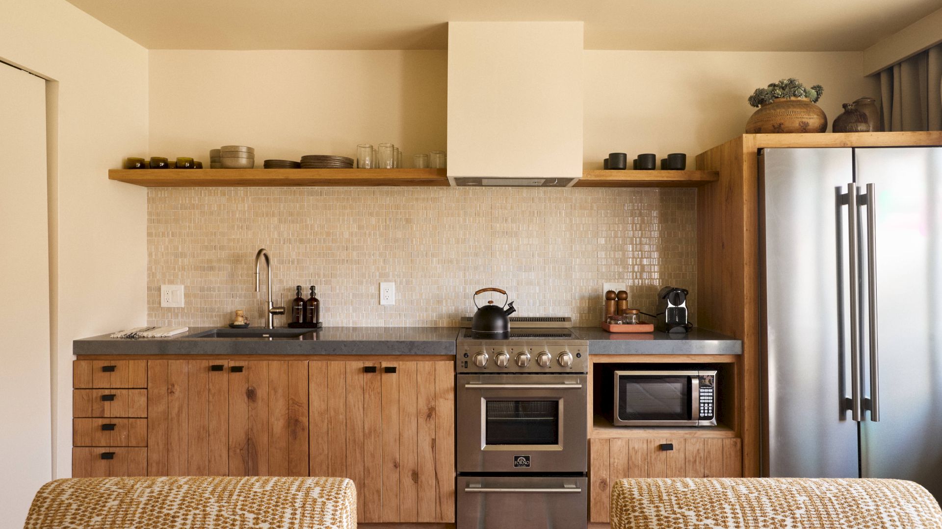 A modern kitchen with wooden cabinets, stove, microwave, coffee maker, refrigerator, and various kitchenware on open shelves and countertops.