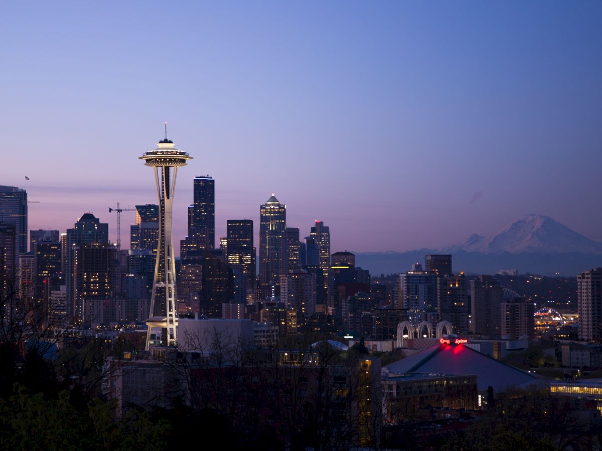 A panoramic view of Seattle's skyline at dusk, featuring the Space Needle and Mount Rainier in the background against a clear sky.